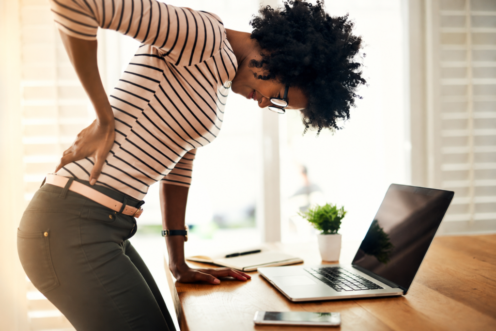 woman experiencing lower back pain while sitting at desk with poor posture during work